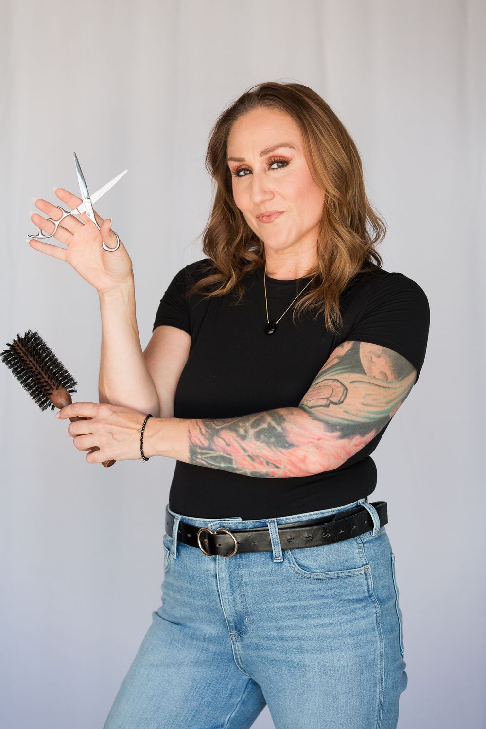 Person demonstrates hairstyling tools and scissors while wearing casual black top and jeans.