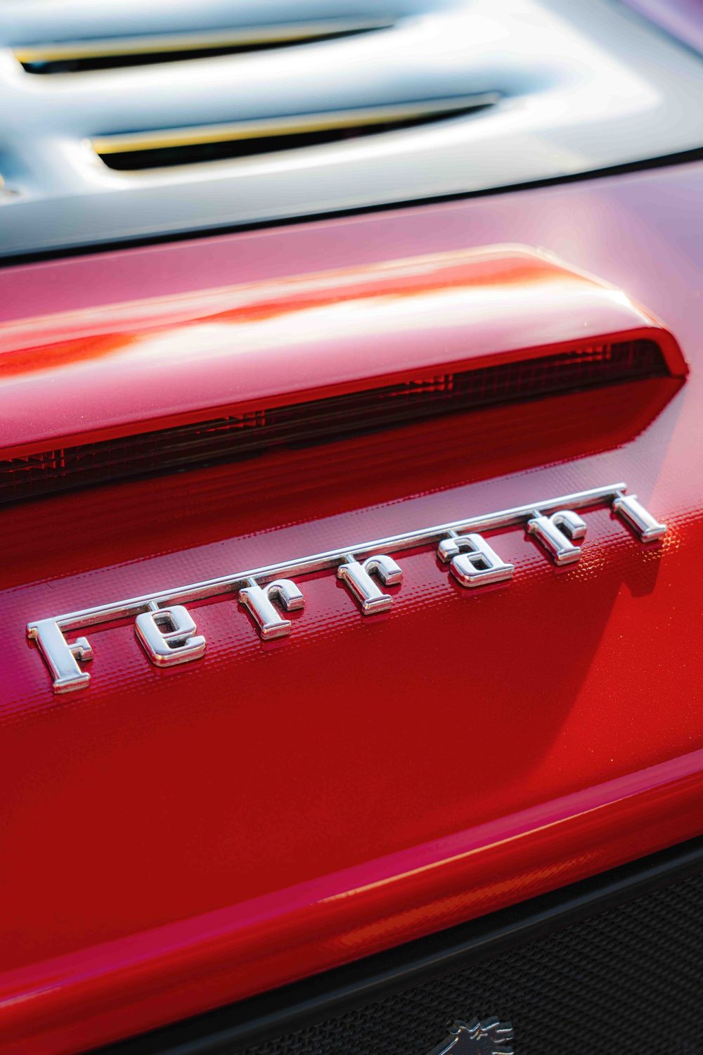 Close-up macro shot of Ferrari lettering on red car body showing metallic chrome badge detail.