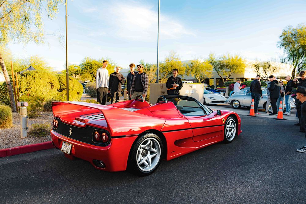 Red Ferrari F40 supercar parked at a car show with other vehicles visible in the background.