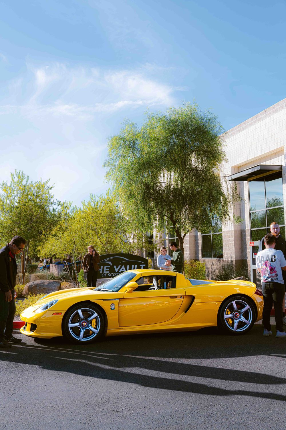 A sleek yellow Porsche Carrera GT supercar shown from multiple angles parked outside a modern building in bright daylight.