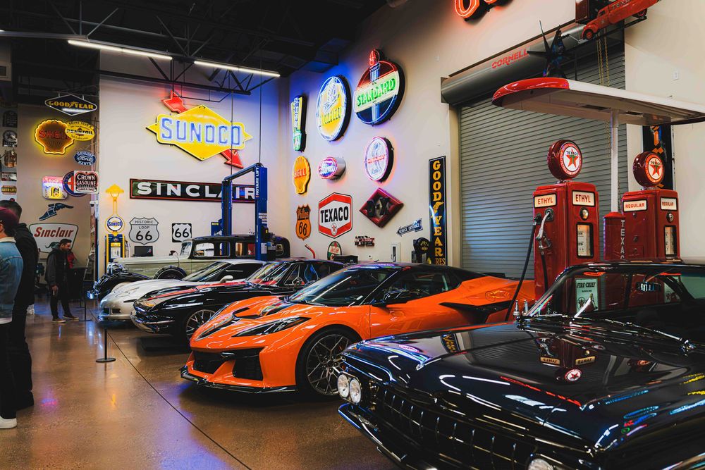 Vintage car showroom displaying luxury sports cars and classic gas pumps with retro automotive signs on the walls.