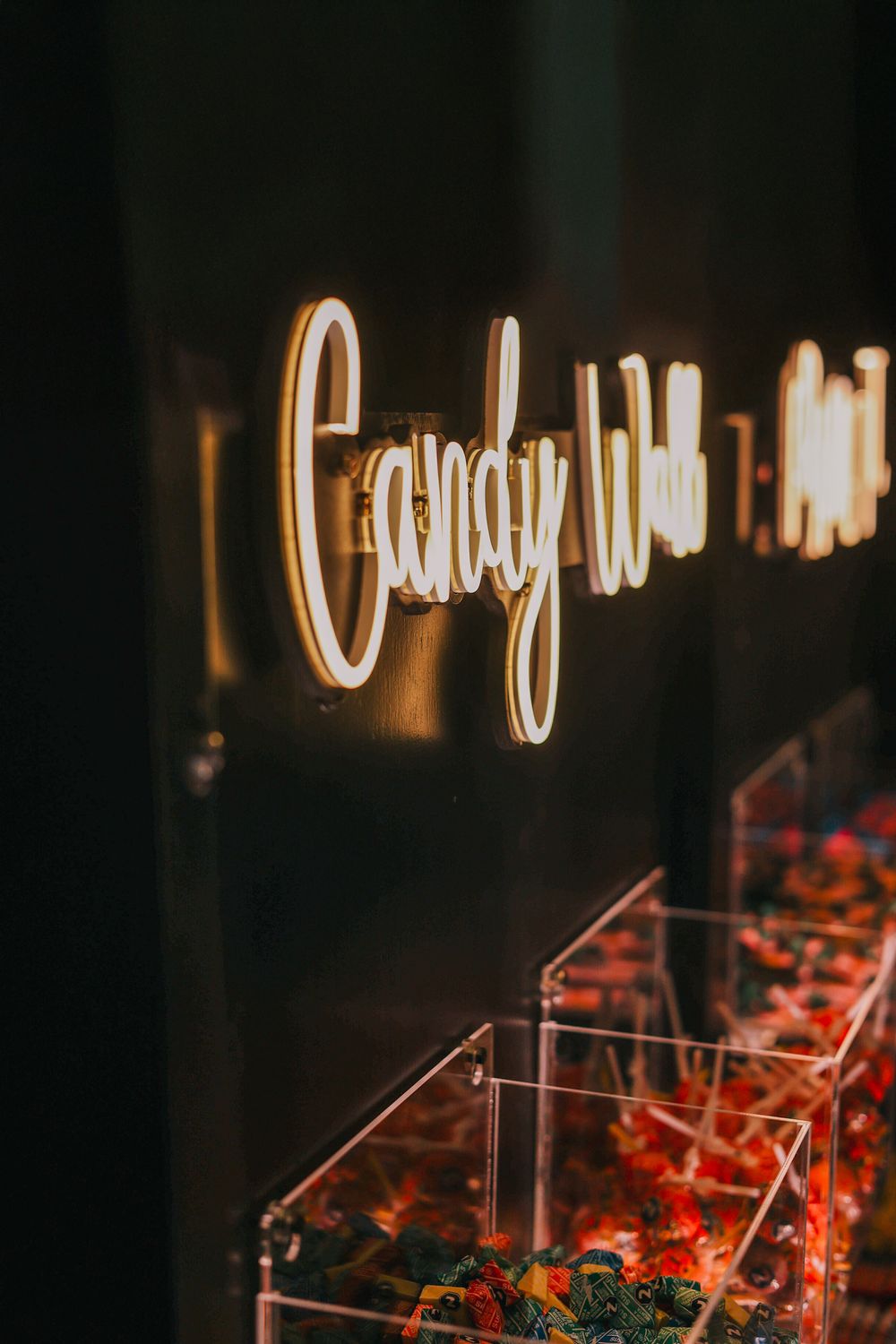 Illuminated neon 'Candy' sign glows warmly above red floral decorations in clear display boxes.