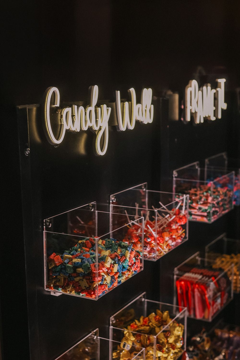 Clear plastic candy dispensers mounted on a dark wall display colorful sweets and treats in modern retail setting.