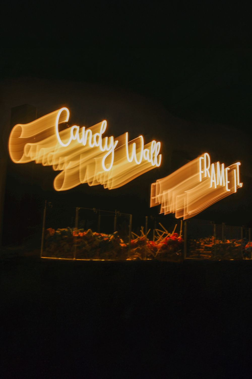 Long exposure photograph of glowing orange light trails against a dark night sky creating illuminated streaks above silhouetted trees.