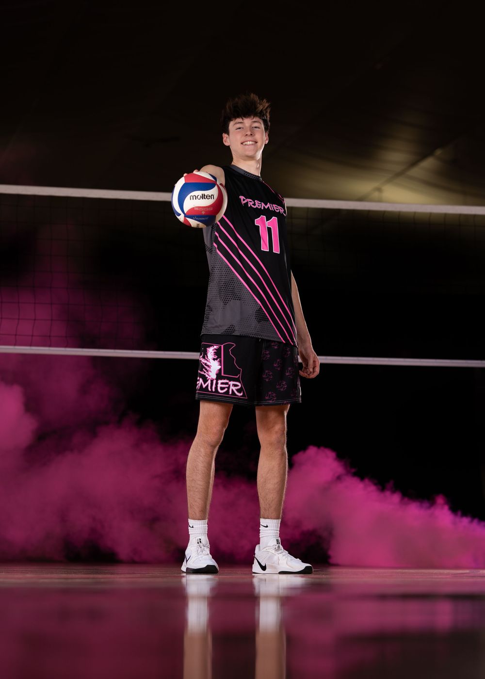 A volleyball player stands on a court with dramatic pink smoke effects creating an atmospheric sports portrait.