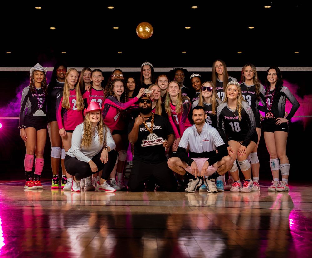 Volleyball team members pose together on a gymnasium floor illuminated by pink lighting during a special event.