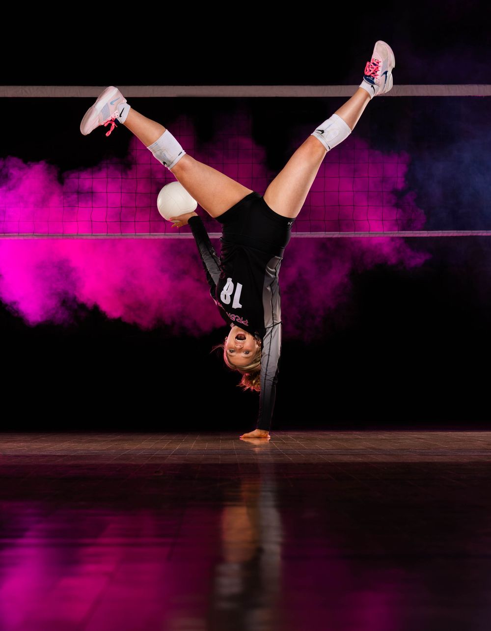 A dancer performs a dynamic breakdancing move with an upside-down handstand against a purple-lit stage backdrop.