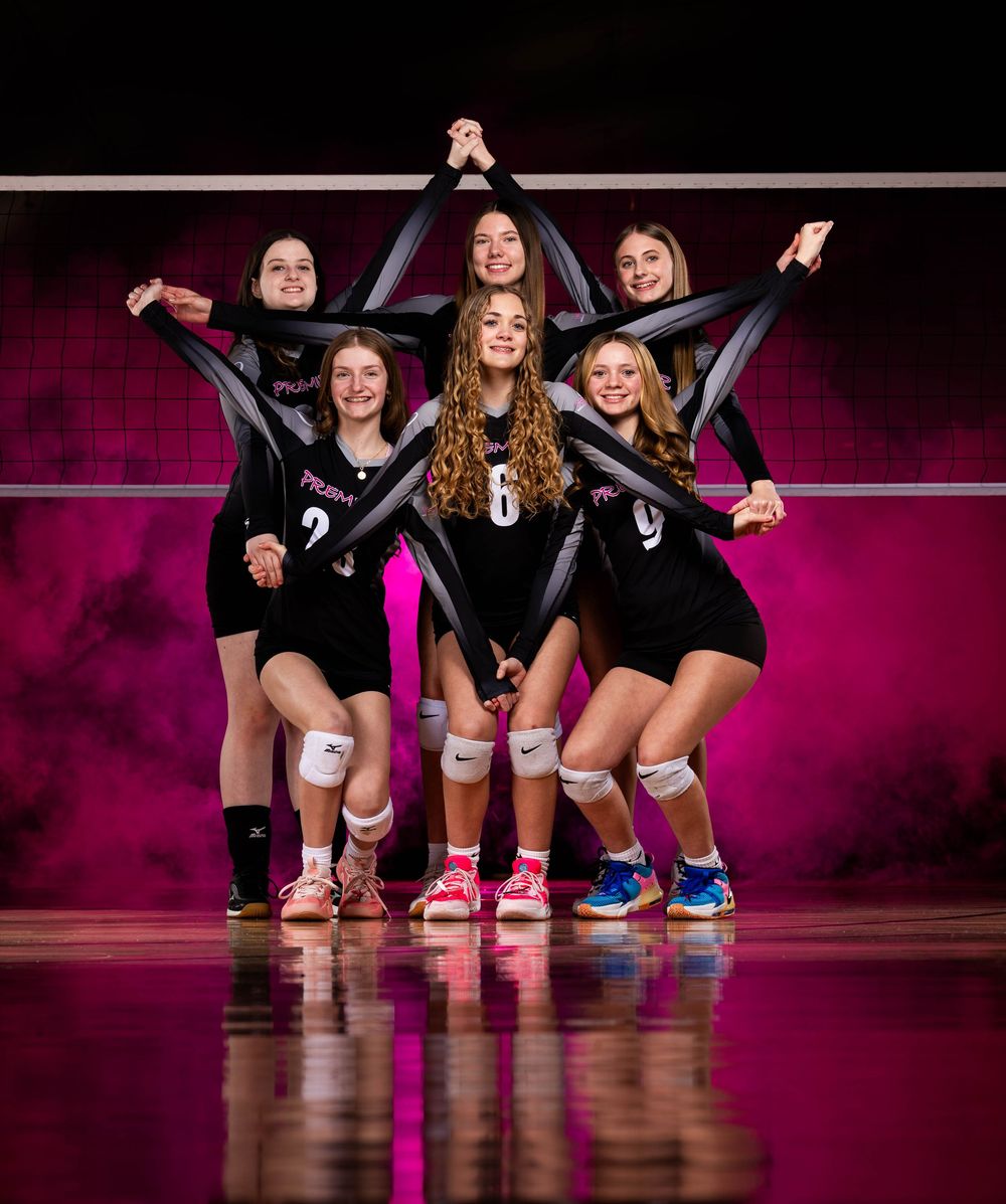 Athletes in black uniforms pose on a volleyball court with pink lighting and colorful sneakers visible.