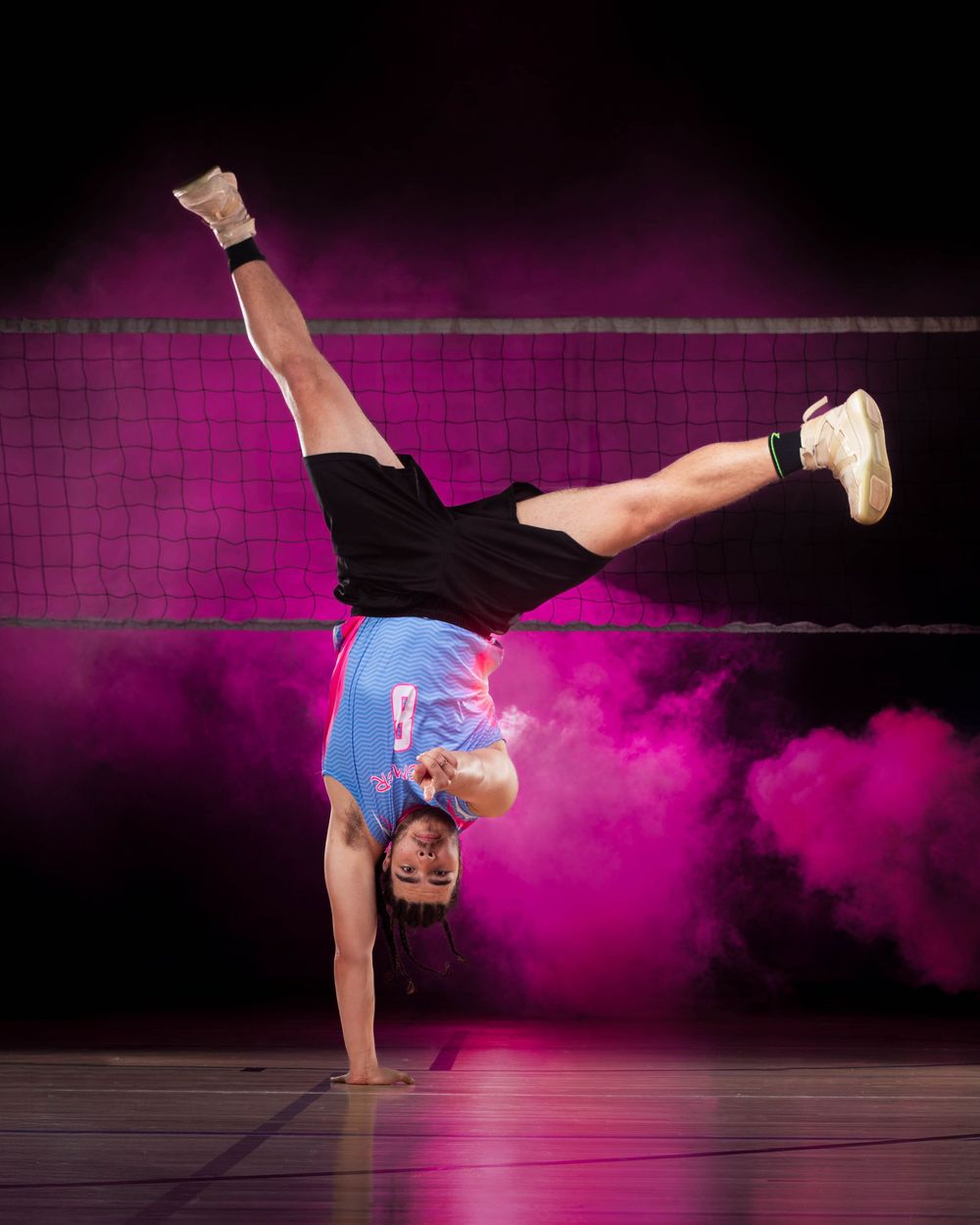 Athletic breakdancer performs dynamic moves against dark background with pink smoke effects.