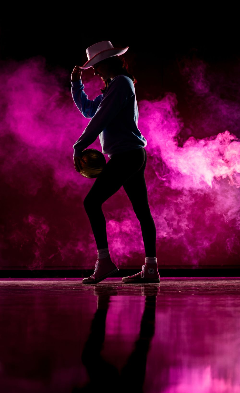 Silhouetted dancer performing against vibrant pink smoke effect on reflective floor in dramatic lighting.