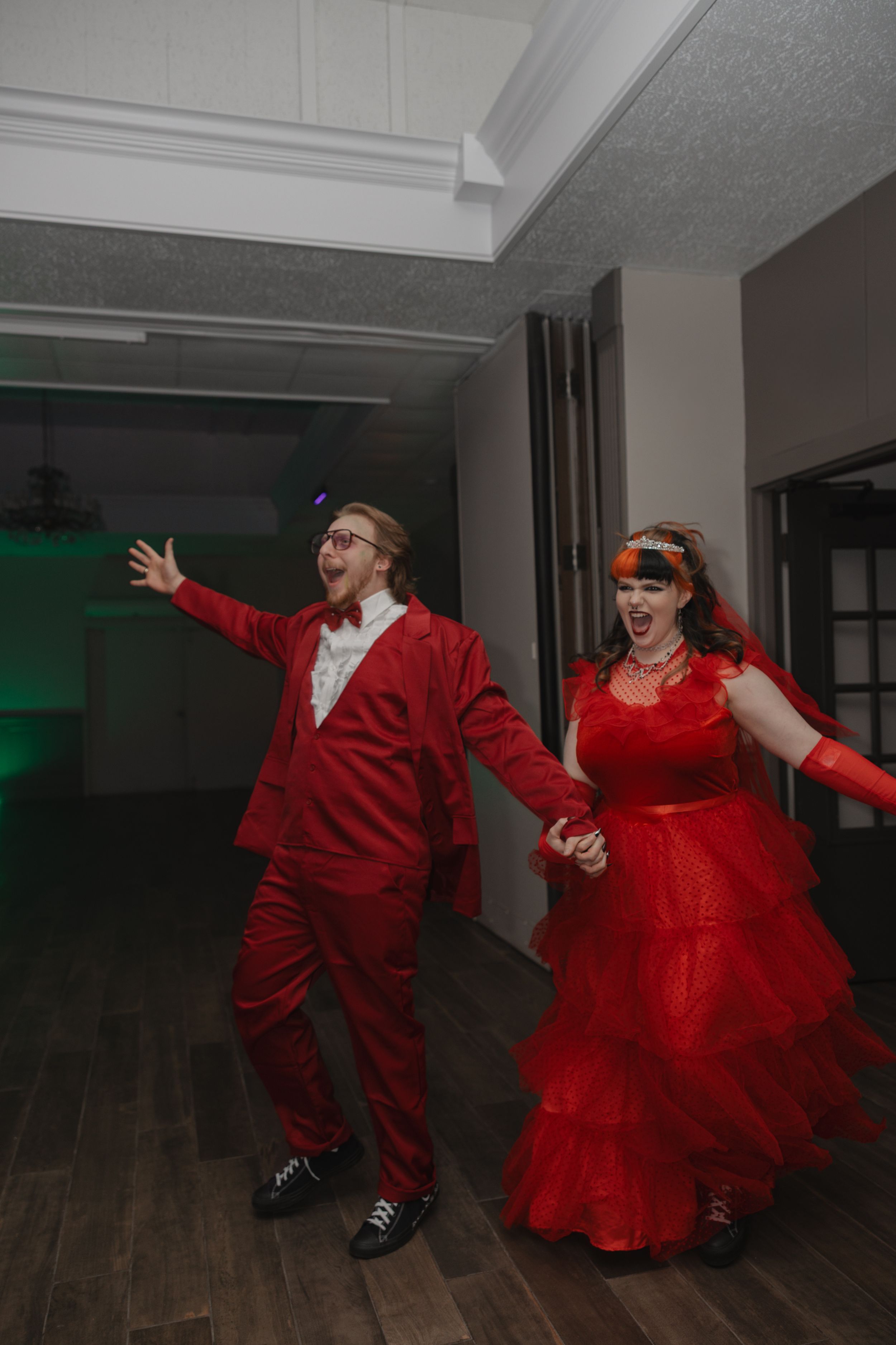 Two people in bright red outfits dance energetically in a dimly lit room with wooden floors.