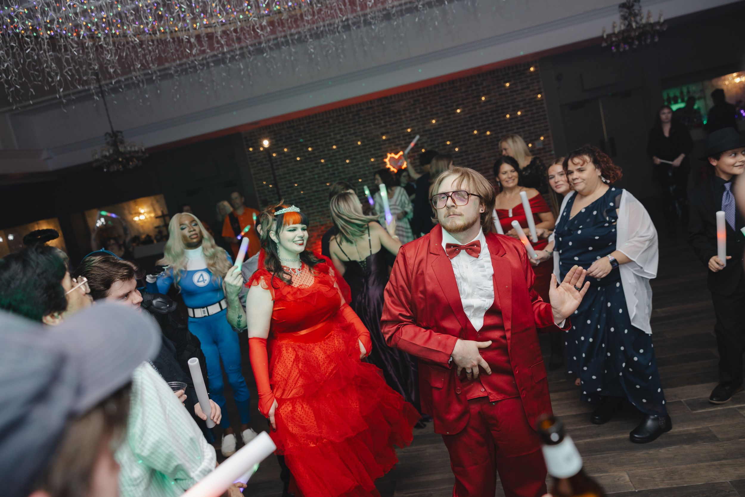 A group of people dance together at an indoor celebration or party venue with festive lighting.