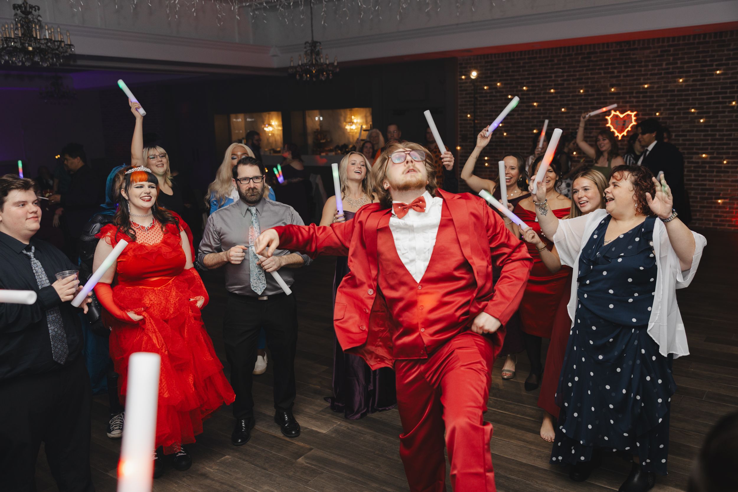 Dancers in red and navy outfits perform energetically at a festive indoor event with twinkling lights in the background.