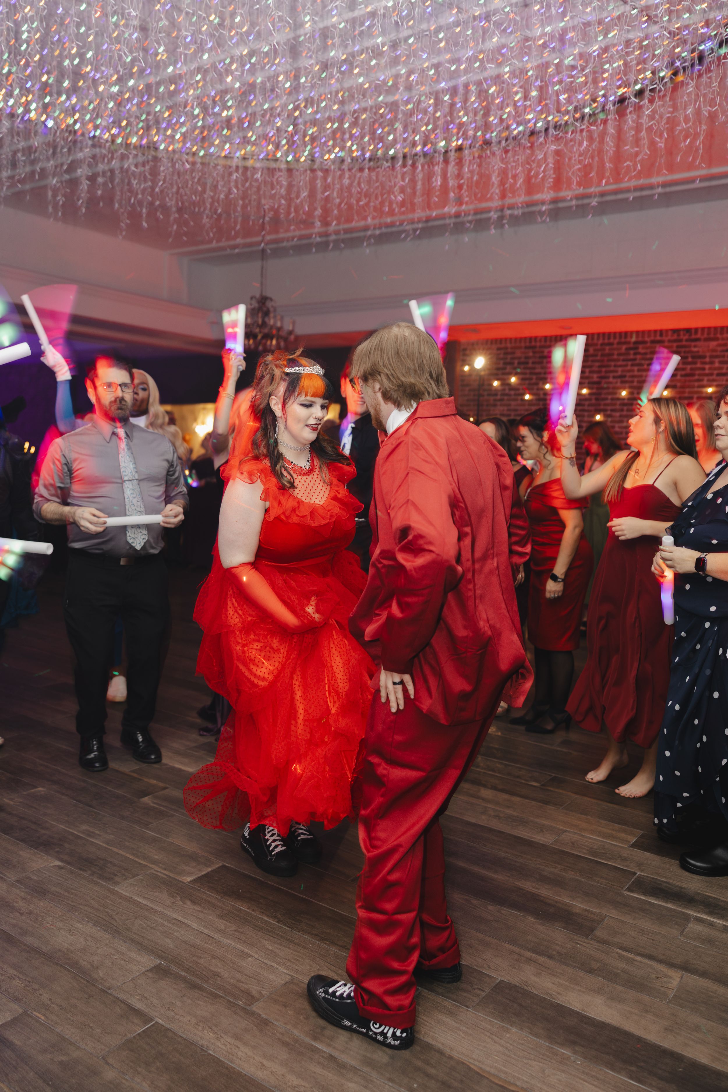 People dancing at a party under sparkling ceiling lights with red illumination on a wooden dance floor.