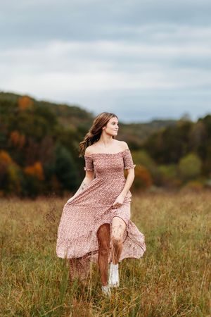 Young woman in floral off-shoulder maxi dress walks through a golden autumn meadow with fall foliage.