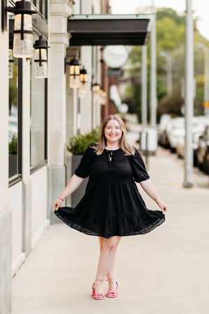 Young woman in black dress twirling on urban sidewalk wearing pink heeled sandals.