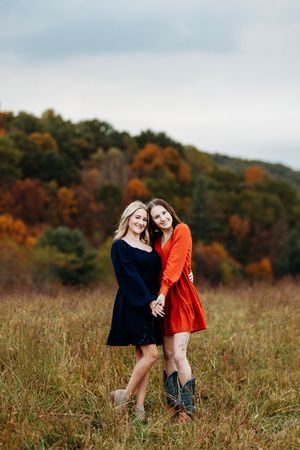 Two young women in navy and orange dresses holding hands in autumn field.