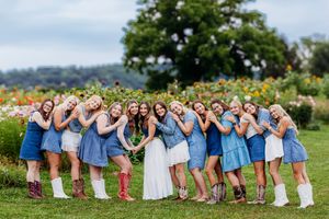 Bride surrounded by bridesmaids in denim dresses and cowboy boots in colorful flower garden.