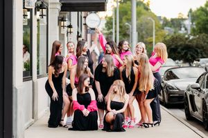 Group of teenage girls in black and hot pink outfits posing together on city sidewalk.