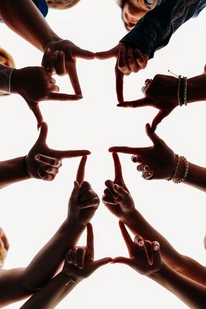 Group of people forming a star shape with their hands and fingers pointing inward, viewed from below.