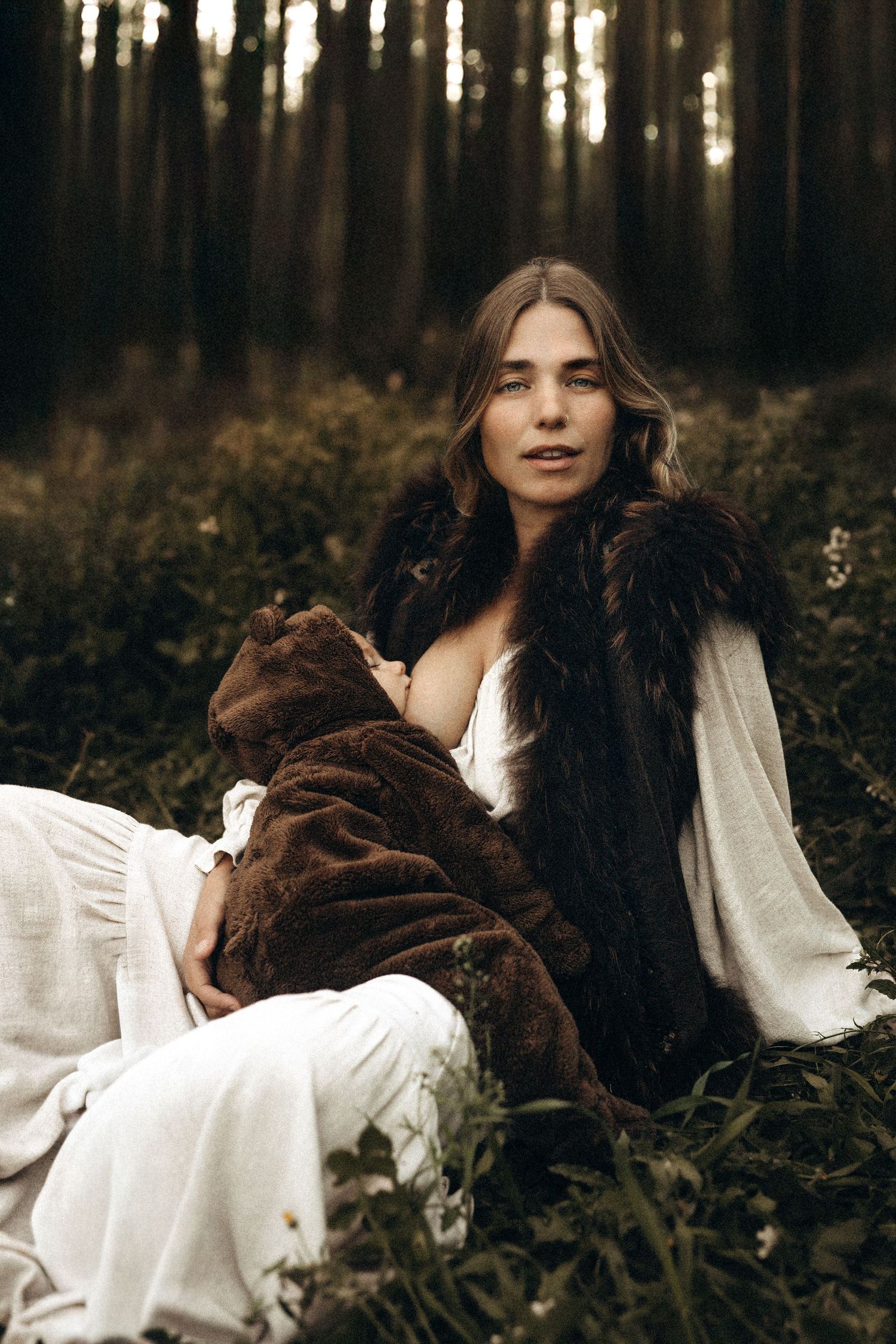 A Mother in a white dress lies among dark ferns in a moody forest setting, creating an ethereal atmosphere. Javea photographer