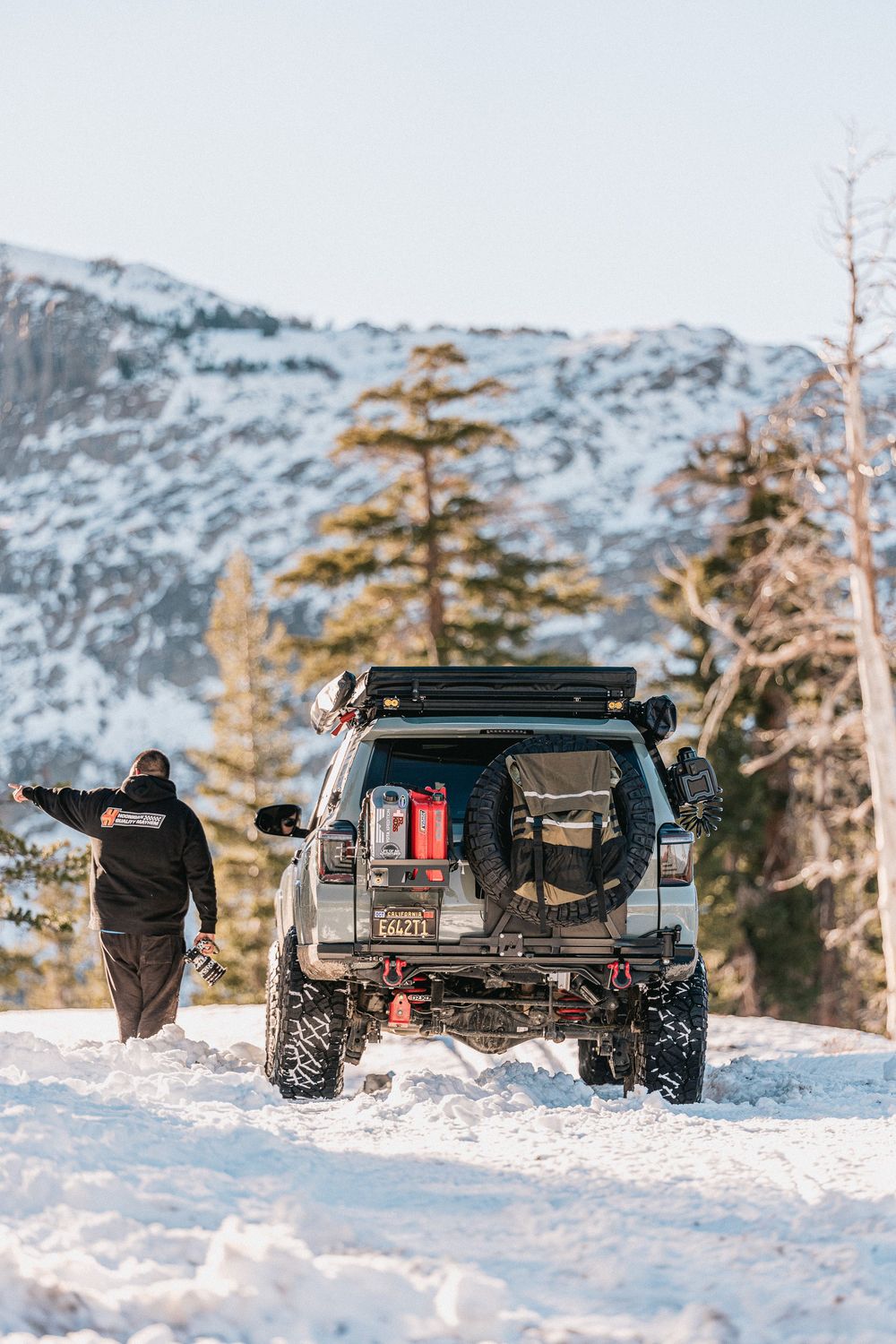Black off-road truck parked in deep snow with mountains and evergreen trees in the winter landscape.