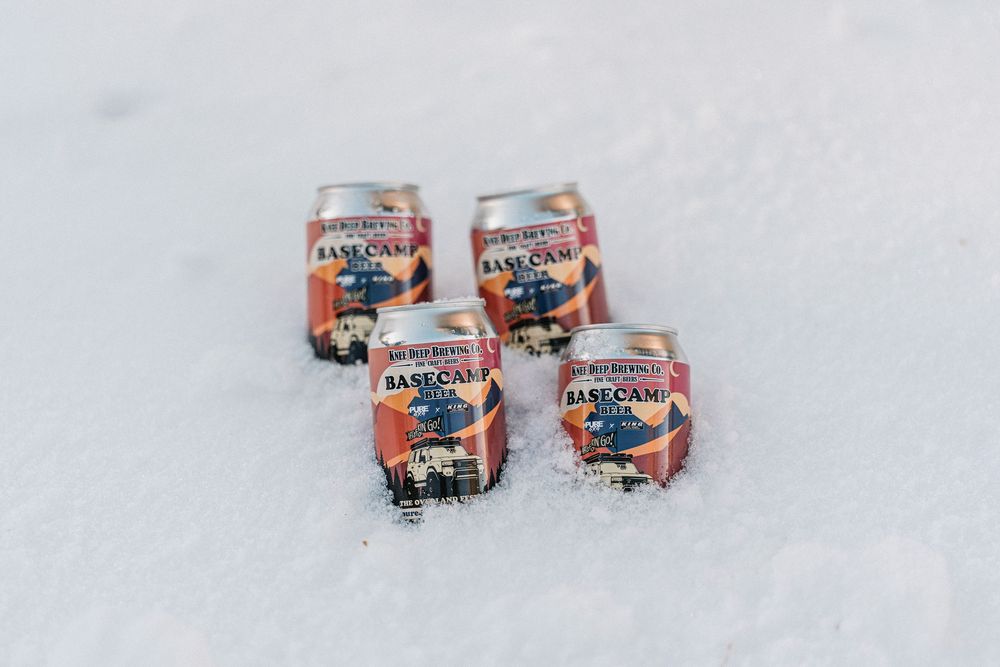Cans of Almanac Beer Co. craft beer nestled in fresh white snow during winter.