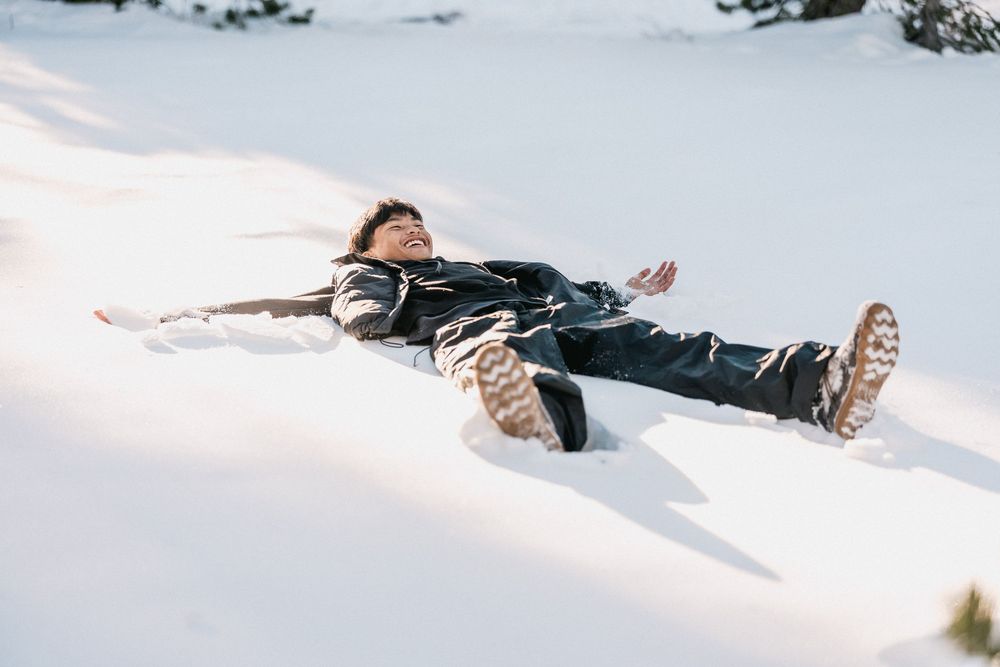 A person lies back in deep snow making a snow angel with their arms and legs spread out in winter.