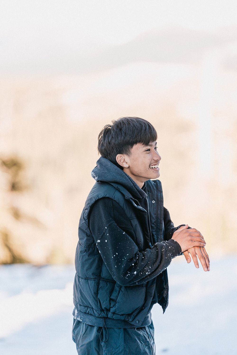 A person wearing a black winter coat laughs joyfully while playing in the snow on a bright winter day.