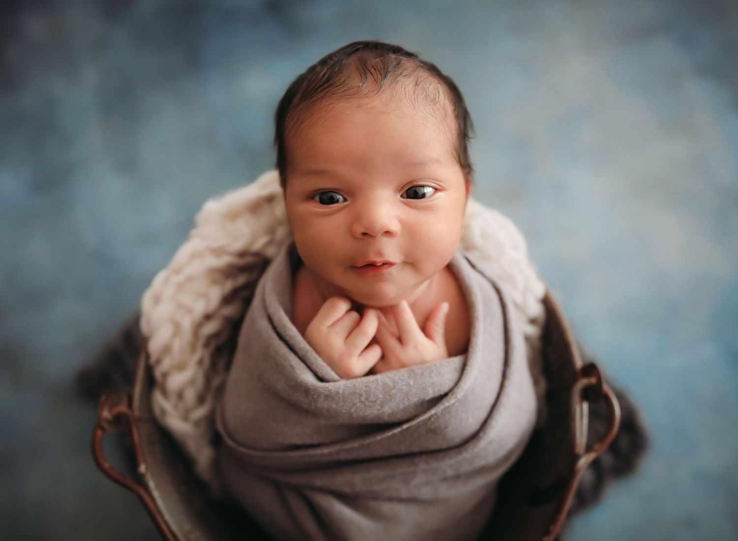 Newborn baby wrapped in soft gray blanket photographed in four artistic close-up portraits.