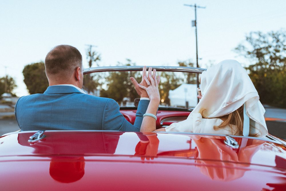 Two people enjoy a scenic drive in a bright red convertible car with their hands raised on a sunny afternoon.