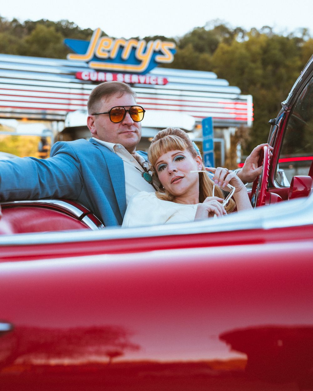 A vintage red convertible car parked at a retro-style drive-in restaurant during sunset.