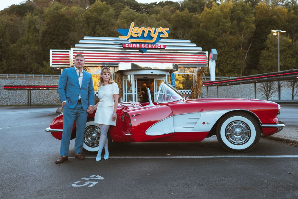 A couple poses with a classic red Corvette outside Jerry's vintage diner at dusk.