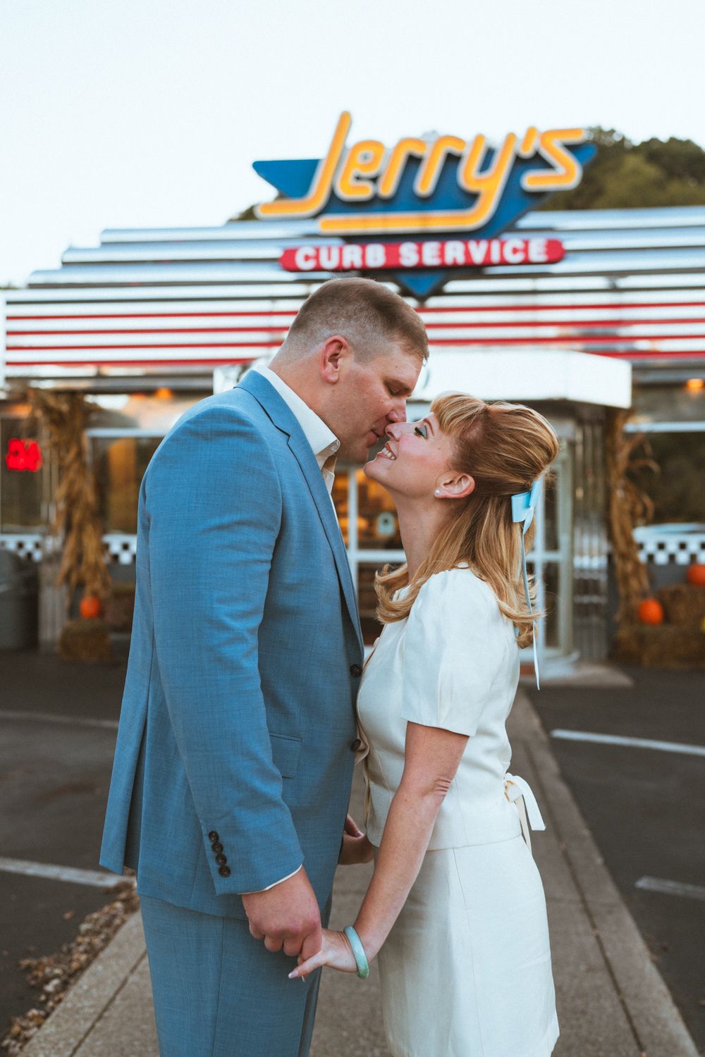 A couple shares a romantic moment outside a retro diner with vintage signage in the background.
