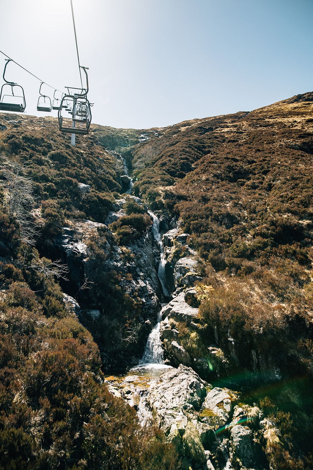 A ski lift runs above a dramatic rocky waterfall cascading down a mountainside in Scotland.