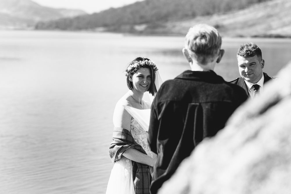 A black and white ceremony photo shows a Scottish wedding by a serene lake in the mountains.