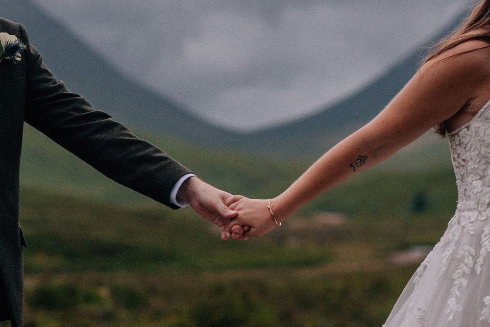 Bride and groom holding hands outdoors with misty mountains in the background on their wedding day.