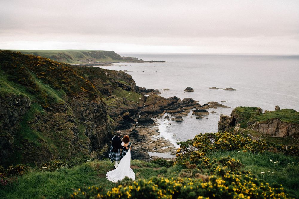 Couple embracing on dramatic Irish coastal cliffs with ocean views and yellow wildflowers during their elopement.