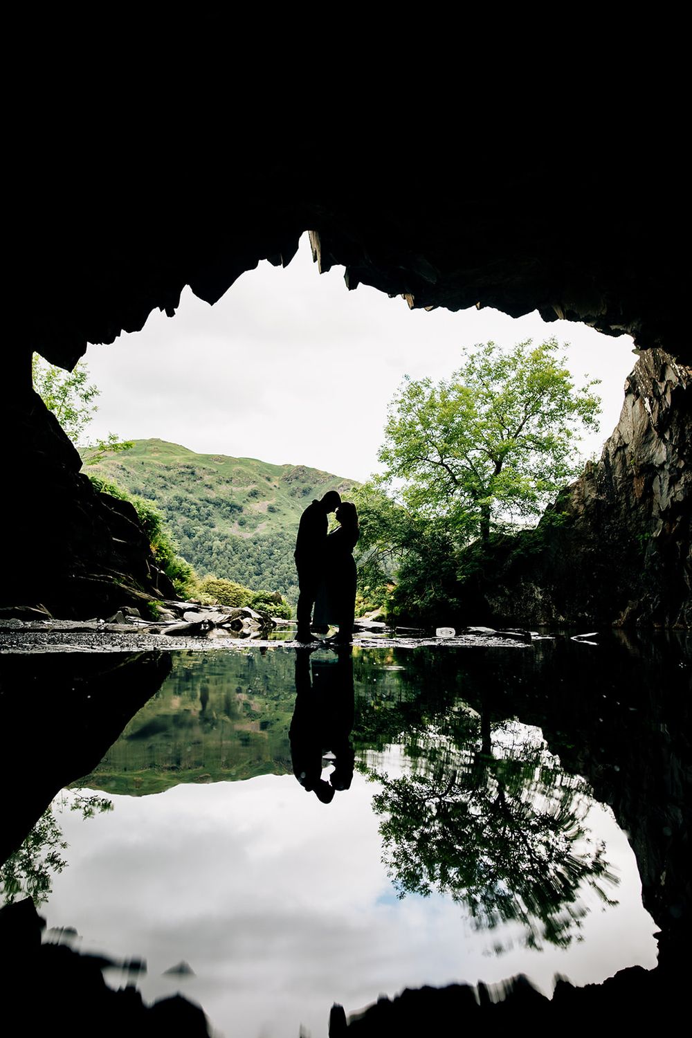 Silhouetted figures in a cave entrance with perfect reflection in still water.