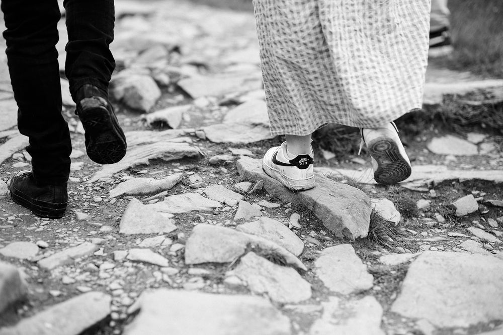 Black and white close-up of two people's feet walking on stone ground.