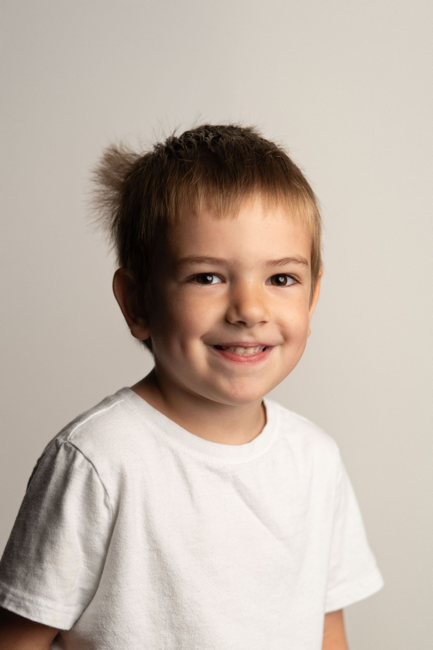 Young child in white t-shirt smiling against neutral background.