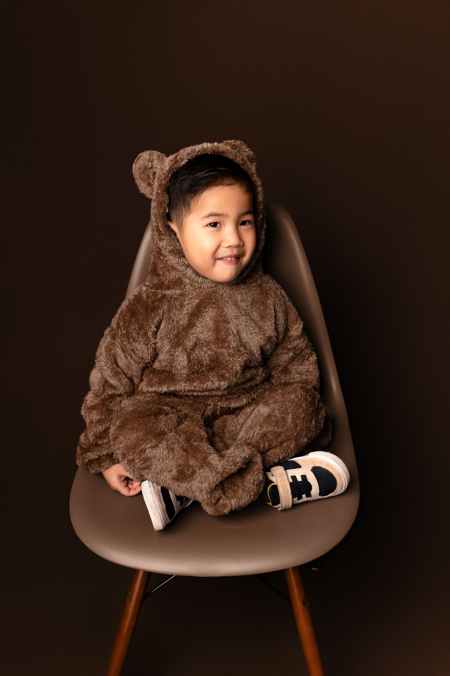 Cozy portraits in a fuzzy brown outfit on a modern chair against dark background.