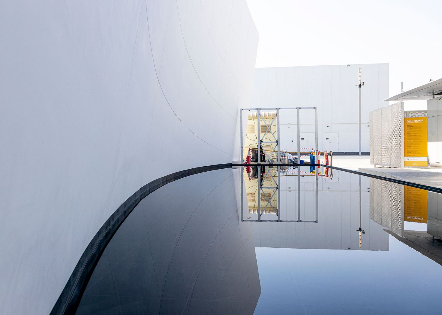 Modern minimalist architecture with curved black wall reflected in still water surface against white building exterior.
