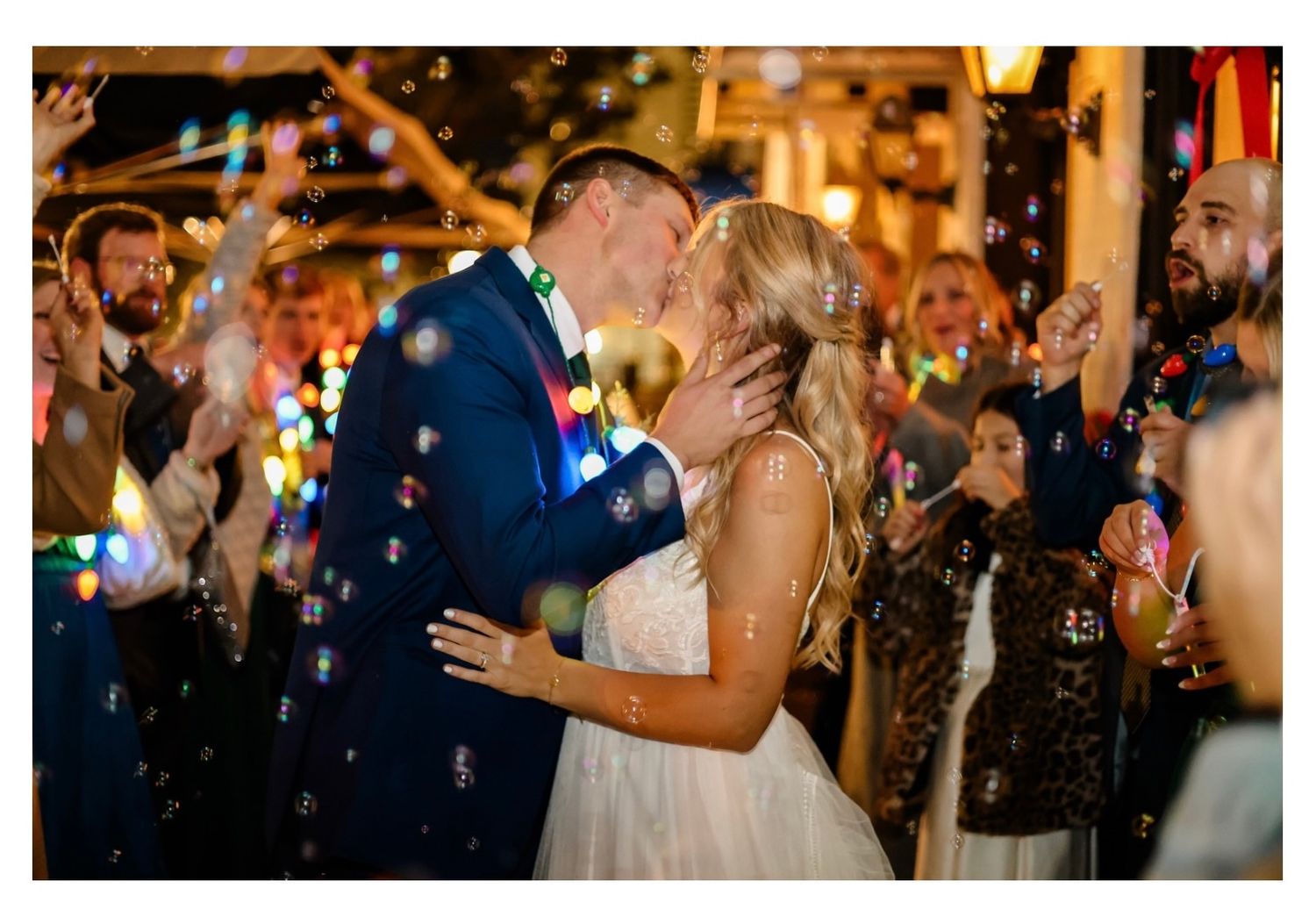 Newlyweds dancing amid bubbles and celebration lights at reception.