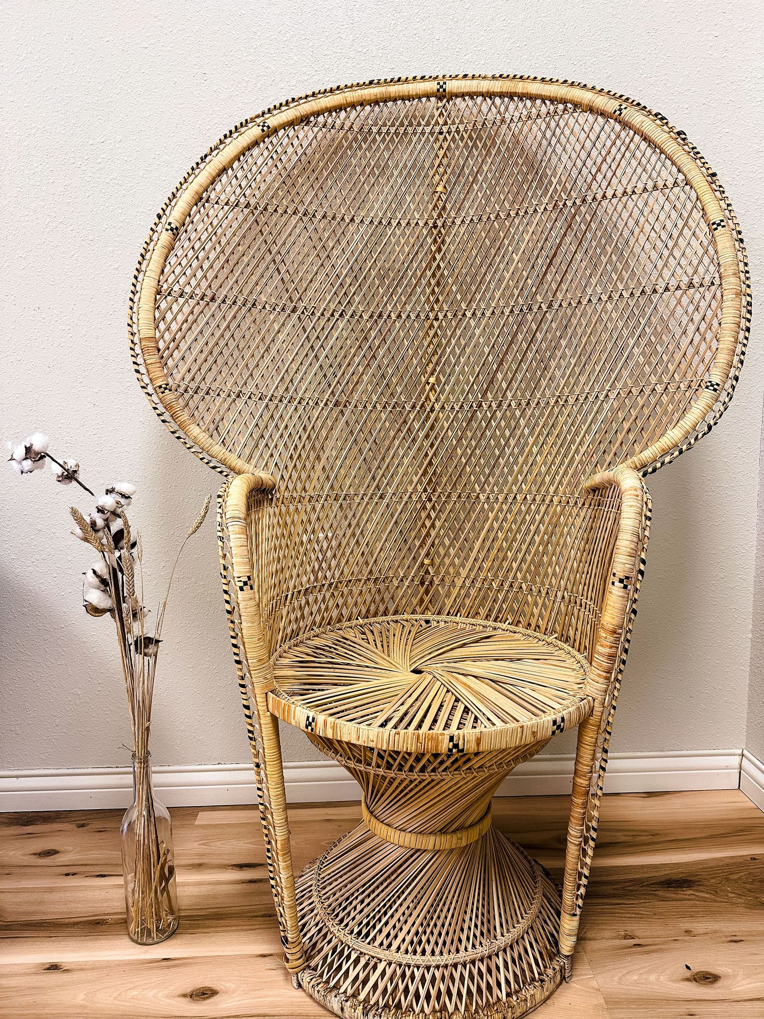Vintage wicker peacock chair with high fan back on wooden floor with minimalist decor and dried flowers.