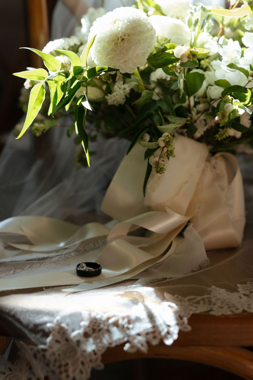 A series of white floral wedding bouquets and decorations arranged on a lace tablecloth with black rings.