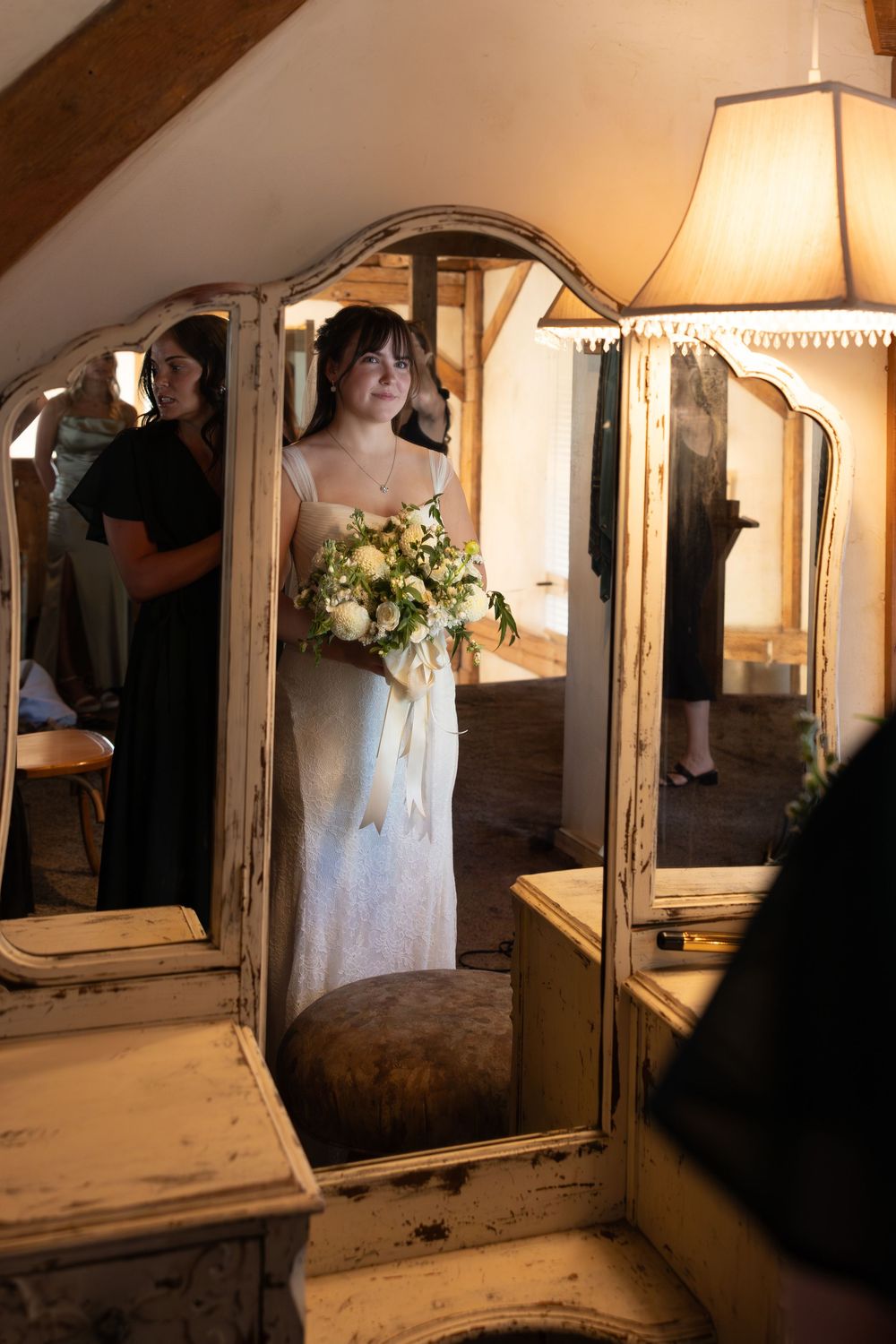A series of vintage mirrors and furniture arranged in a dimly lit room with soft lamp lighting and floral accents.