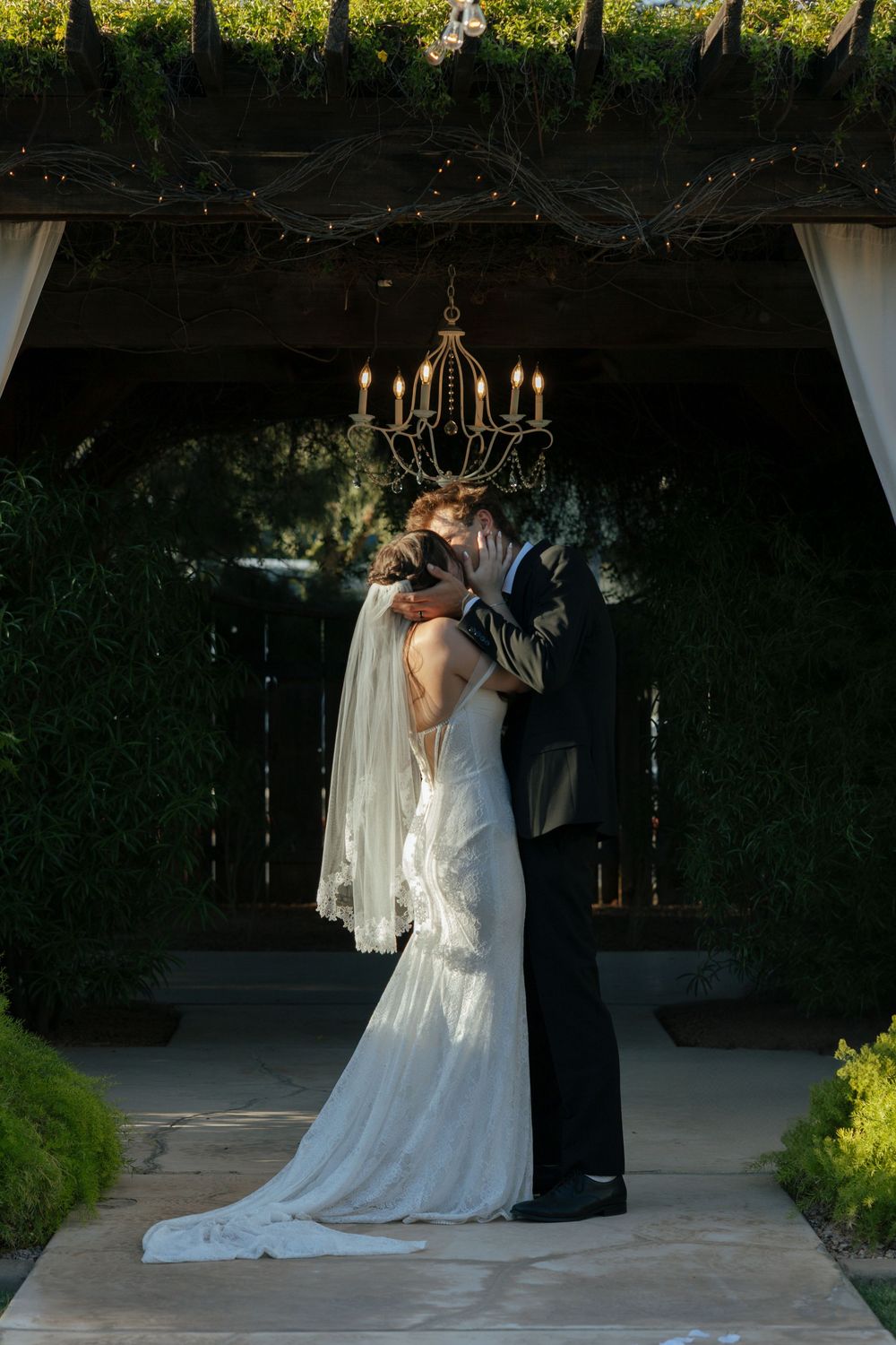 A couple shares their first kiss under an elegant chandelier in a garden wedding venue.