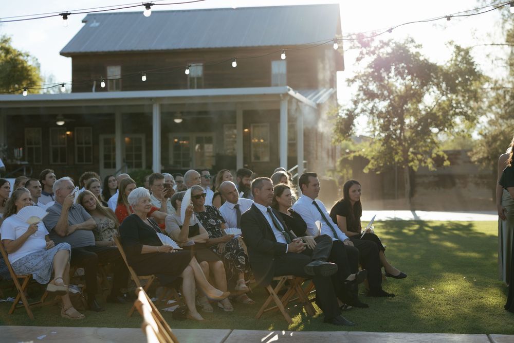 People gather on a porch at sunset to enjoy an outdoor social event with string lights overhead.