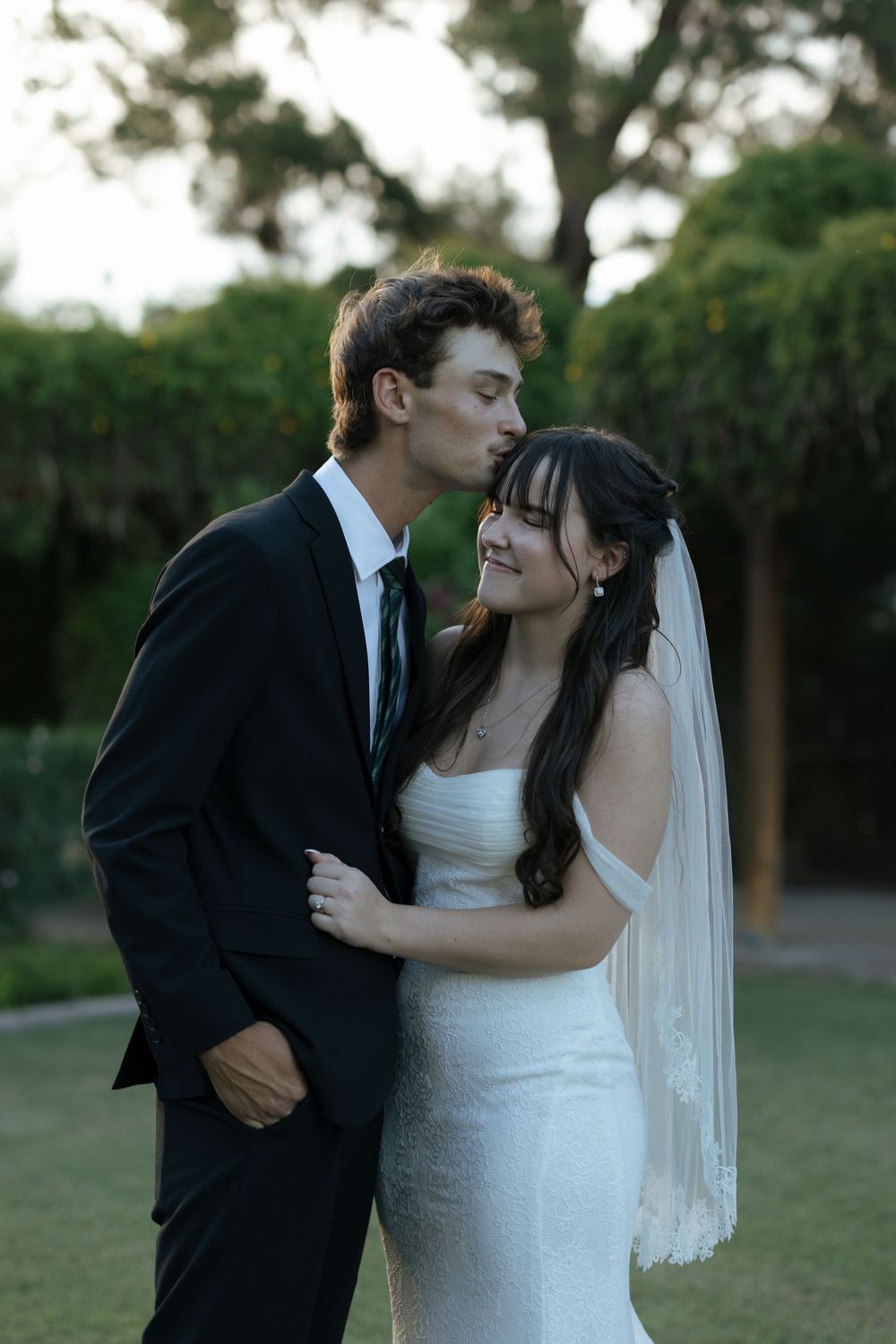 A romantic wedding moment captured outdoors with a couple in formal attire sharing an intimate embrace.